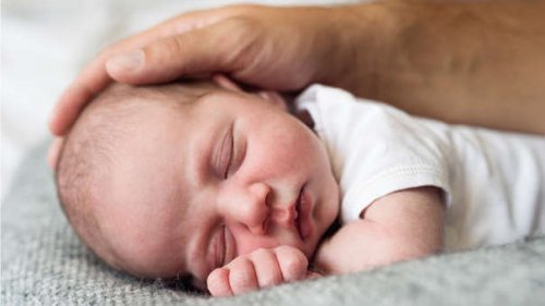Un bébé qui dort avec une main d'adulte qui le caresse