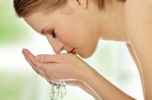 Une femme qui se rince le visage avec de l'eau pour avoir un maquillage naturel