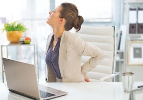 Une femme assise au bureau qui a mal au dos à cause de la discopathie dégénérative