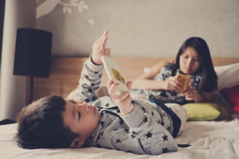Deux enfants allongés sur un lit avec un téléphone portable.