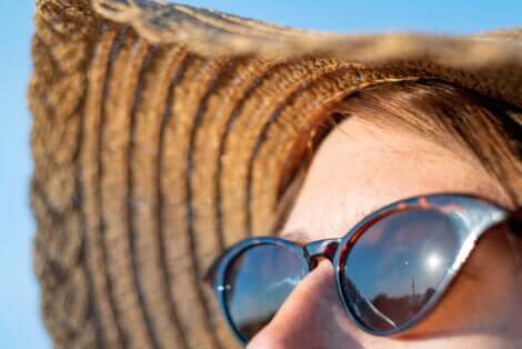 Le visage d'une femme au soleil avec des lunettes et un chapeau pour se protéger de la radiation solaire.