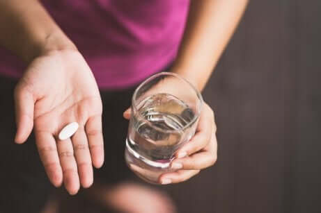 Un comprimé de paracétamol dans une main avec un verre d'eau. 