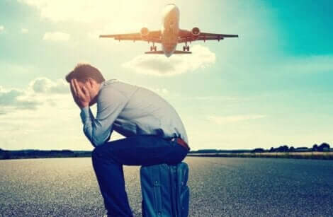 Un homme assis sur sa valise devant un avion qui décolle. 