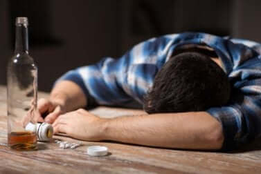 Un homme endormi sur une table qui a bu une bouteille d'alcool entière. 