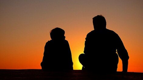 Un père et son fils devant un coucher de soleil. 