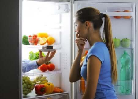Une femme devant un frigo ouvert qui hésite entre un fruit et une part de gâteau au chocolat. 
