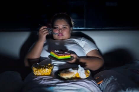 Une femme obèse qui mange des pâtisseries devant la télé. 