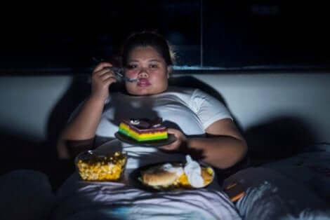 Une femme obèse qui mange des pâtisseries devant la télé.