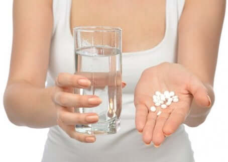 Pastilles de médicaments dans une main avec un verre d'eau. 
