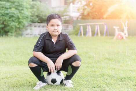 Un enfant assis sur un ballon en tenue de football. 