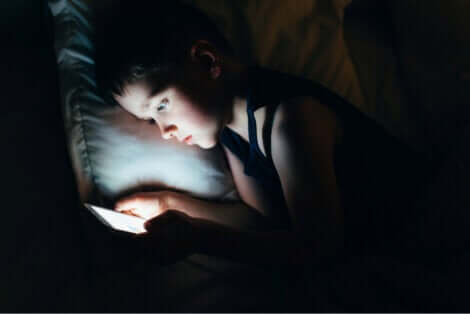 Une jeune fille qui regarde son téléphone au lit pendant la nuit.