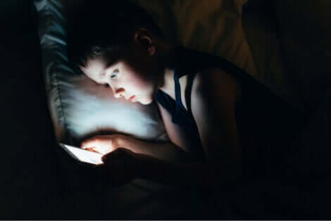 Une jeune fille qui regarde son téléphone au lit pendant la nuit. 