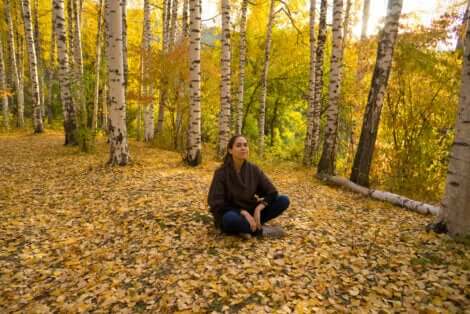 Une femme assise au sol qui médite dans une forêt.