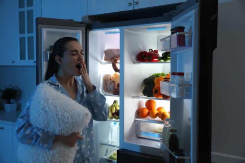 Une femme avec son oreiller devant son frigo en pleine nuit.